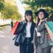 Portrait of happy girls shopaholics standing outdoors with bright bags, looking at camera and smiling touching hair. Shopping, people and modern youth lifestyle concept.