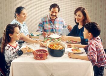 Family Eating Meal. A Hispanic family (male adult, two female adults, female child, and male child) enjoy a meal at the dinner table.