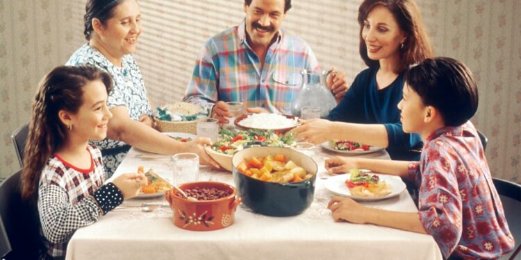 Family Eating Meal. A Hispanic family (male adult, two female adults, female child, and male child) enjoy a meal at the dinner table.