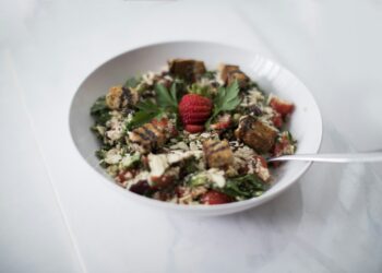 Schaal met parelcouscous, paprika en platgedrukte gehaktballetjes met yoghurtsaus