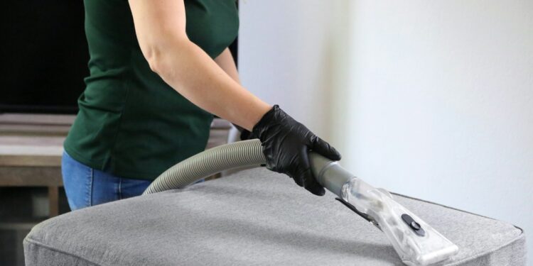Handstuk van een tapijtreiniger dat over de zitting van een grijze stoffen bank gaat