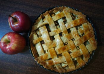 Appeltaart met een gevlochten deegrooster en karamel die langs de rand druipt
