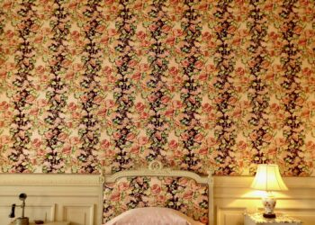 Muur met behang met grote botanische bladeren en bloemen achter een bed
