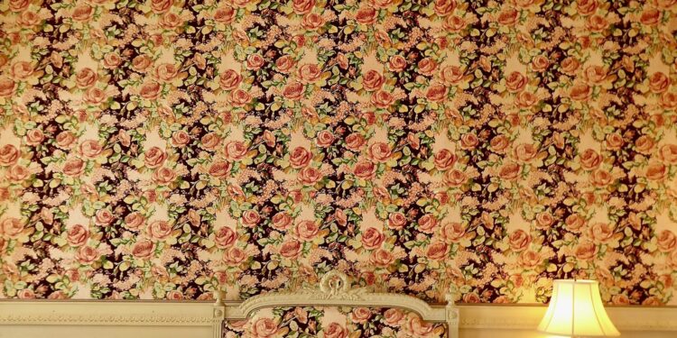 Muur met behang met grote botanische bladeren en bloemen achter een bed