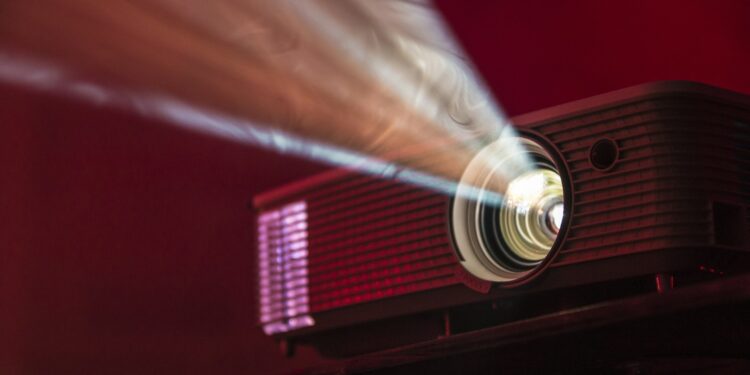 Projector die een film op een witte muur projecteert in een donkere woonkamer