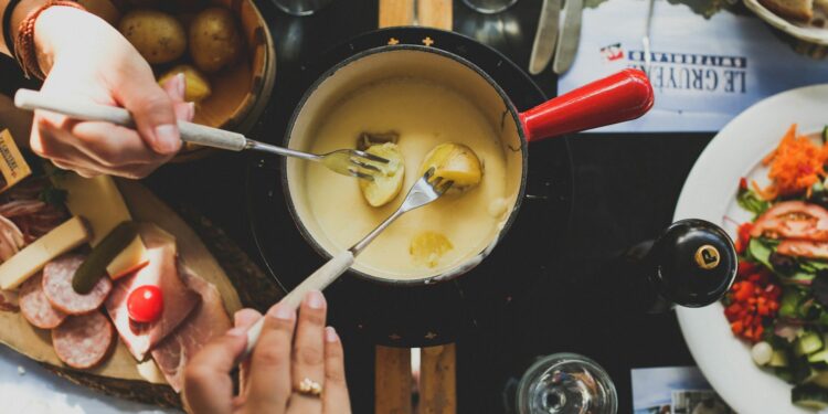 Pan met gesmolten kaasfondue en stukjes brood op fonduevorkjes
