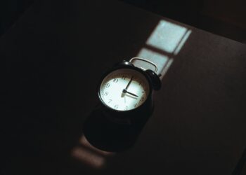 Wekker op een nachtkastje naast een bed in een schemerige slaapkamer