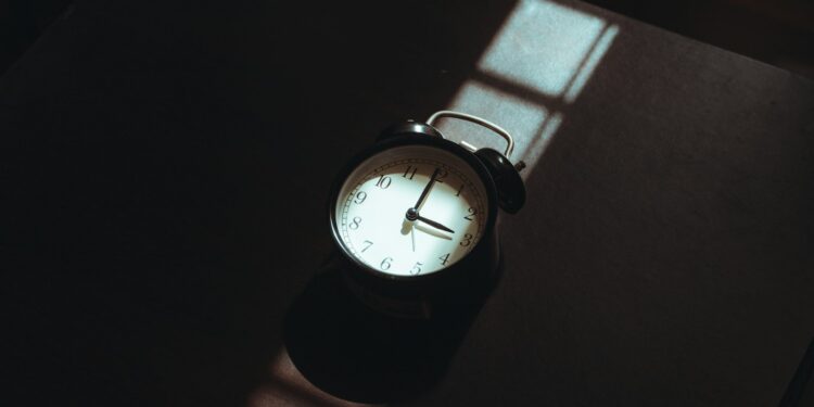Wekker op een nachtkastje naast een bed in een schemerige slaapkamer