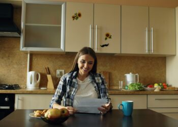 Vrouw van middelbare leeftijd schrijft aan de keukentafel aantekeningen in een notitieboekje