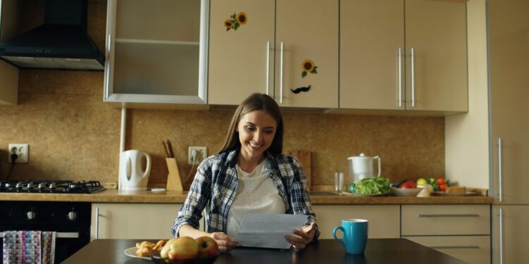 Vrouw van middelbare leeftijd schrijft aan de keukentafel aantekeningen in een notitieboekje