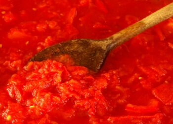 Hele gepelde tomaten uit blik in een kom naast een pan met tomatensaus