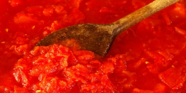 Hele gepelde tomaten uit blik in een kom naast een pan met tomatensaus