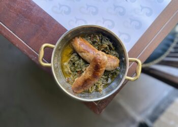 Pan met boerenkoolstamppot en plakjes rookworst op een houten keukentafel