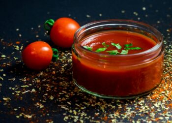 Tomatenpuree in een kommetje naast verse tomaten op het aanrecht