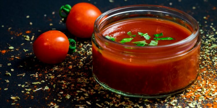 Tomatenpuree in een kommetje naast verse tomaten op het aanrecht