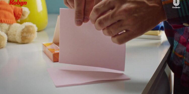 Hand scheurt een roze wasmiddeldoekje van Robijn doormidden boven de wasmachine