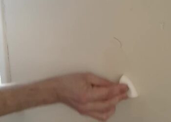 Hand wrijft met een witte wonderspons een vlek van een lichte muur