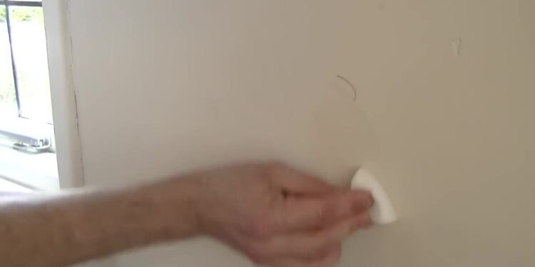 Hand wrijft met een witte wonderspons een vlek van een lichte muur
