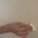 Hand wrijft met een witte wonderspons een vlek van een lichte muur