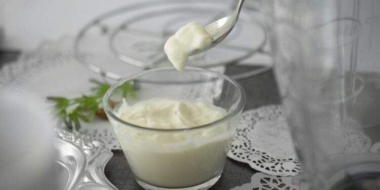 Glazen pot met zelfgemaakte yoghurt en een houten lepel op tafel